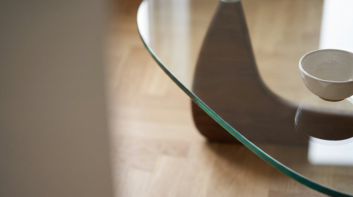 Polished edge of a clear glass table top catching soft morning light, with a ceramic bowl