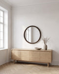 Enso round wall mirror Ø 70 cm with dark wood frame above a light oak sideboard in a bright living room