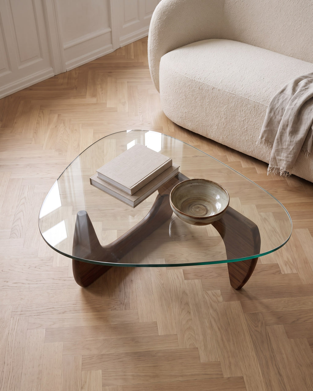 Elara walnut coffee table seen from above, sculptural wooden base visible through the clear glass top