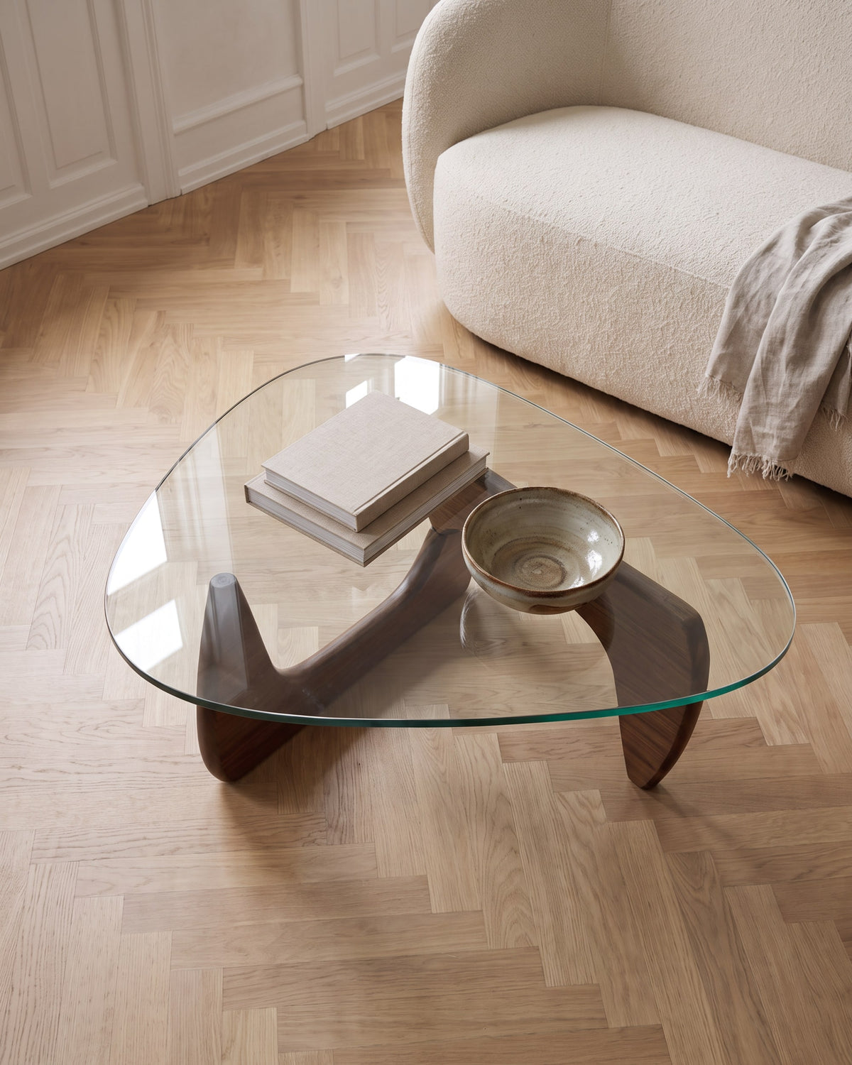 Elara walnut coffee table seen from above, sculptural wooden base visible through the clear glass top