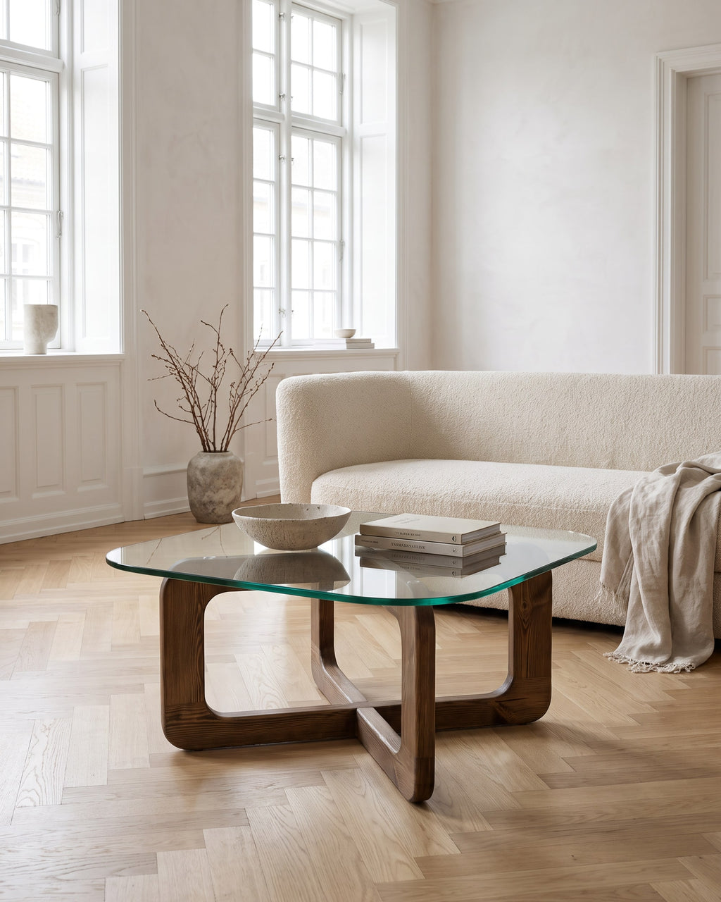 Couchtisch Vesta mit abgerundet-quadratischer Glasplatte und Kreuzgestell in Walnuss-Optik in einem hellen Wohnzimmer