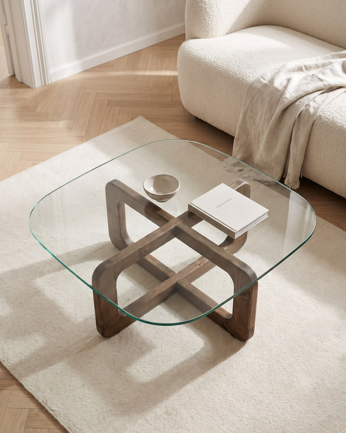 Vesta coffee table seen from above, cross-shaped walnut-finish base visible through the glass top