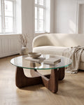 Selene round coffee table with clear glass top and sculptural walnut-finish cross base in a bright living room