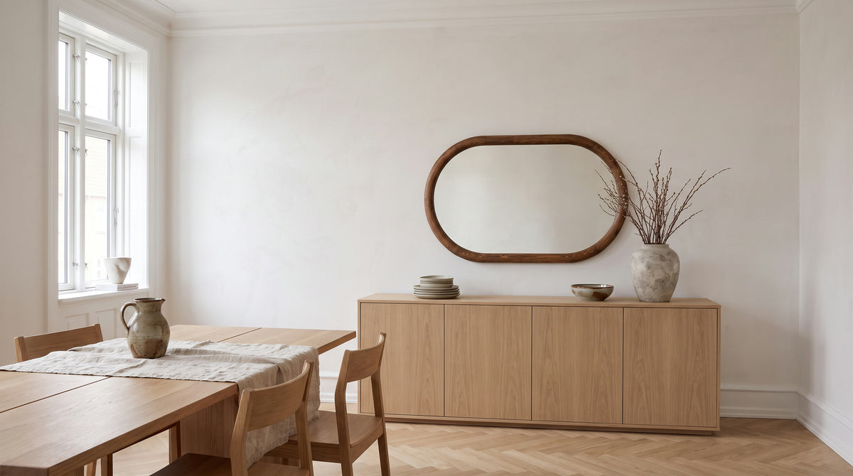 Light dining room with a pill-shaped walnut mirror above a long oak sideboard and an oak dining table