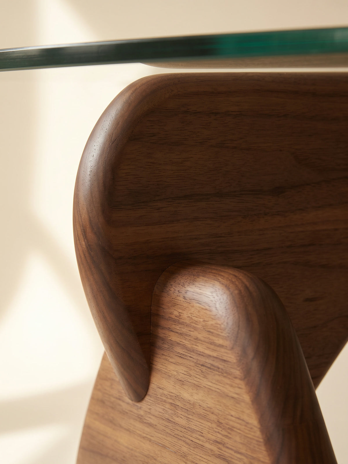 Close-up of walnut-stained wood grain on a sculptural table base beneath a glass top